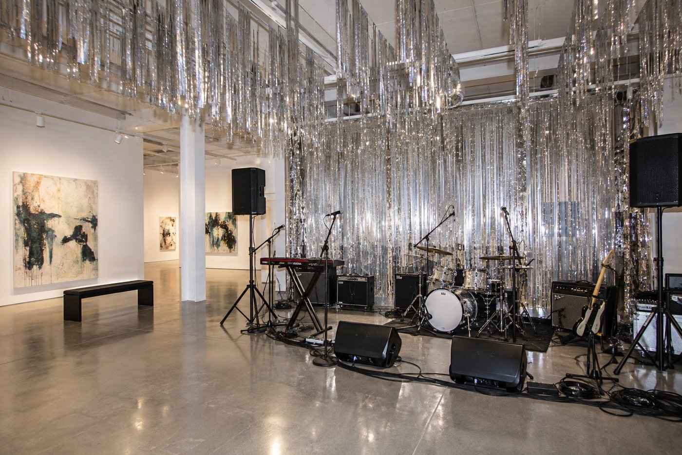 Source-grounded editorial illustration of silver streamers and a small live-performance setup in a white gallery